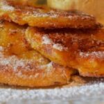 Goldbraun gebackene Apfel-Zimt-Pfannkuchen auf einem Teller, bestäubt mit Puderzucker