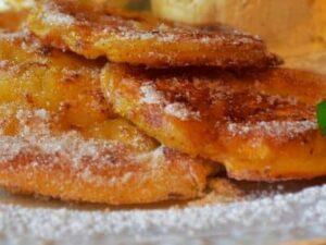 Goldbraun gebackene Apfel-Zimt-Pfannkuchen auf einem Teller, bestäubt mit Puderzucker