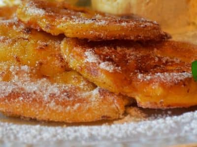 Goldbraun gebackene Apfel-Zimt-Pfannkuchen auf einem Teller, bestäubt mit Puderzucker
